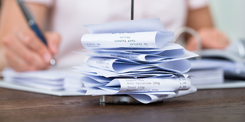 receipts stacked on a desk with a woman writing in the background
