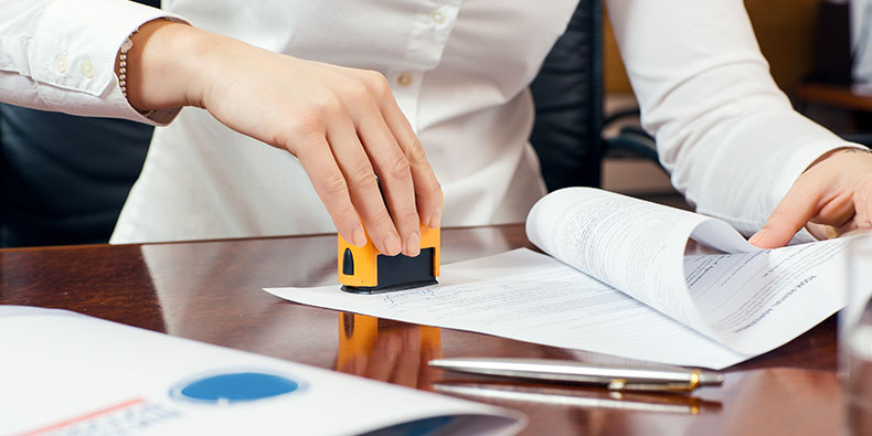 closeup of a woman in a white blouse using a stamp on a document