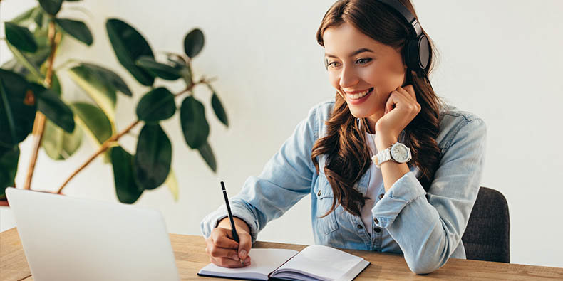 A woman wearing a headset sitting in front of a laptop taking notes